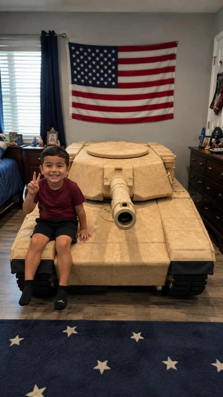 A young boy sitting on a large tan military tank model in a child's bedroom, making a peace sign. An American flag hangs on the wall behind him.